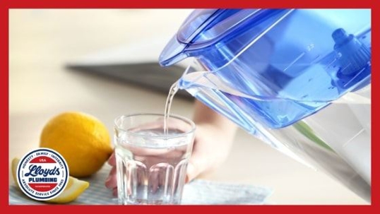 A blue and clear water pitcher pouring water into a glass next to a lemon